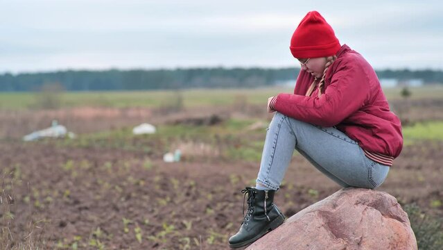 A sad teenage girl sits on a rock in a field and cries.