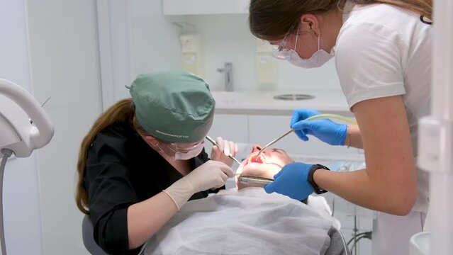 hard tooth extraction, tooth extraction tools Gracie curette, piezo scaler, piezo scaler attachment, piezo scaler wrench, luxator woman doctor dentist removes a man patient tooth heavy easy extraction