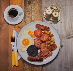 Full cooked breakfast and cup of coffee shot from above, the food is on a wooden table.