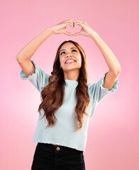 Naklejka premium Happy, heart hands and shape with woman in studio for romance, positive and kindness. Love, support and emoji with female and smile isolated on pink background for emotion, hope and gesture