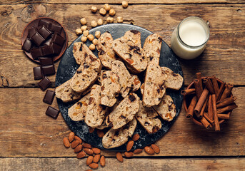 Board with delicious biscotti cookies, nuts, chocolate and glass of milk on wooden background