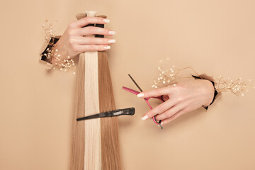 Hands with flowers hold strands of hair for extensions on a beige background.