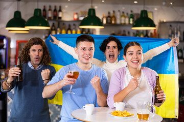 Obraz premium Happy friends of different ages drinking beer and celebrating the victory of the Ukrainian team in the night bar
