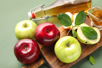 Glass bottle of fresh apple cider vinegar and board with fruits on green background