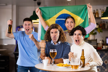 Happy friends of different ages drinking beer and celebrating the victory of the Brazilian team in the night bar