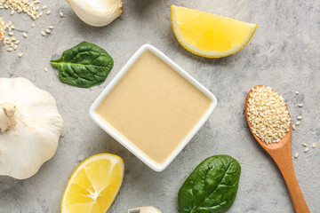 Composition with tasty tahini, sesame seeds, garlic, spinach and lemon slices on grunge background, closeup