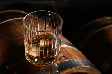 Oak barrels with glass of cold whiskey on dark background