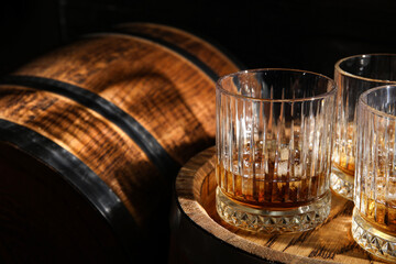 Oak barrels with glasses of cold whiskey on dark wooden background - obrazy, fototapety, plakaty