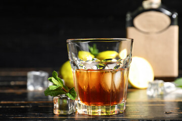 Glass of rum with ice cubes on dark wooden background