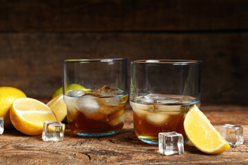 Glasses of rum with ice cubes and lime on wooden background