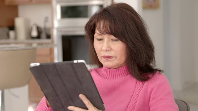 Closeup stylish mature woman in pink using mobile tablet sitting indoors at home