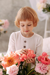 Child Blonde 6-7 years old in a white dress holds pale pink flowers in her hand. The concept of congratulations on March 8, flower shop or greenhouse, botanical garden or environmental protection.