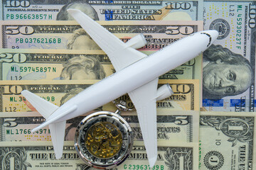 Passenger plane and pocket watch sitting on US currency bills of different denominations showing concept high cost of flying, time  - obrazy, fototapety, plakaty