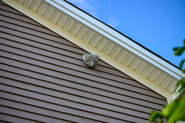 A large wasp hornet nest is affixed to an exterior dryer vent cover on the eave of a wooden building. The pesky insects are on the outside of the papery pulp type material hexagonal comb with a hole. 