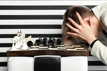 An angry and upset woman gesticulates with her hands while sitting at a chessboard. Emotional defeat in the game.