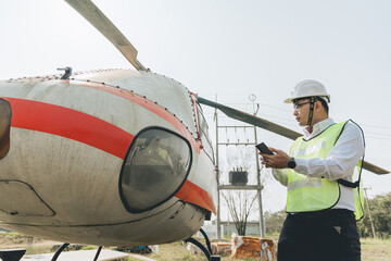 Asian man Aero Engineer Working On Helicopter In Hangar Looking At Digital Tablet