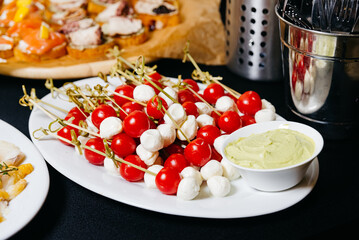 tasty appetizer with mozzarella and cherry tomatoes on skewers and dipping sauce the table. big...