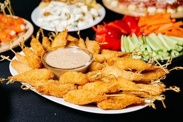 Fried shrimps breaded on skewers with nutty sauce on a plate, among appetizers, finger food and sliced fresh vegetables