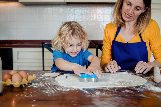 Family cooking: Kid son and mother preparing cookies at home kitchen - Soft focus on child face