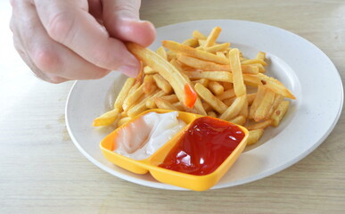 Person's hand and potato chips with mayo and ketchup close up.