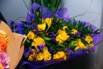 Bouquet of yellow roses and purple flowers in a purple wrap