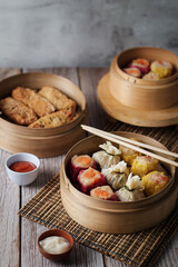 dim sum dumplings in bamboo steamer with sauce on wood table