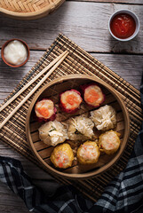 dim sum dumplings in bamboo steamer with sauce on wood table. top view