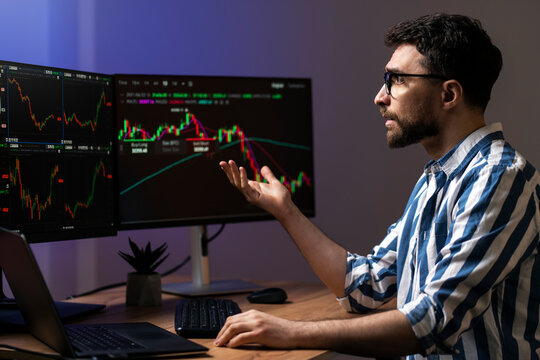 Frustrated man, crypto trader looking at computer monitor, working online with crypto chart sitting in modern office. Online trading concept