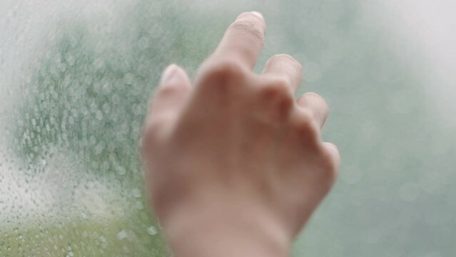 何かを掴むように雨の滴で濡れた窓の外に向けて手を伸ばす女性