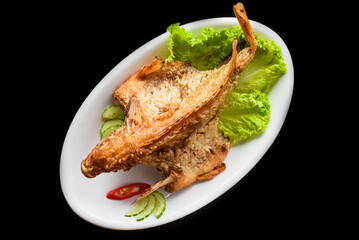 Fish grilled in batter with vegetables and greens on white plate isolated on black background side view