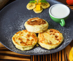Syrniki or cheese pancakes with cream sauce and bananas on a plate on wooden table close up