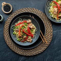A meal of chicken pieces with edamame beans, red peppers and black sesame seeds.