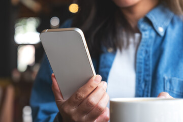 Closeup image of a young woman holding and using mobile phone in cafe