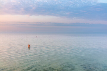 Fototapeta na wymiar Young woman in brown swimwear going into the sea on the beach at sunrise