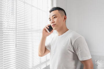 Asian man is taking a call near the window.