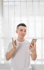 Asian man is using mobile phone near the window shades.