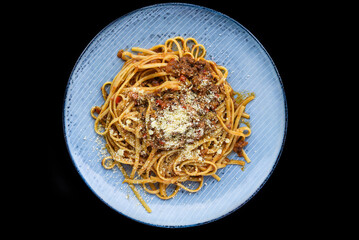 Pasta bolognese on blue plate 
 isolated on black background top view 