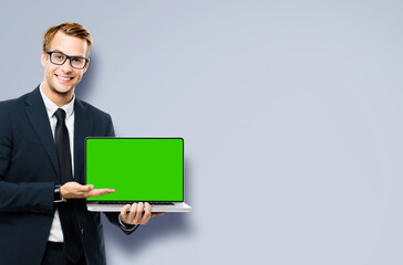Business man in glasses spectacles, black suit show laptop with empty mockup green chroma key screen, isolated grey gray background. It expert,  technician repair service, tech support maintenance