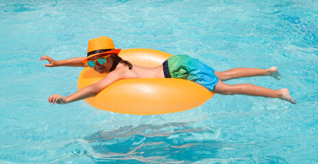 Fototapeta na wymiar Smiling cute little girl in sunglasses and summer hat in pool in sunny day. Child splashing and swimming in pool. Swim water sport activity on summer vacation with child.