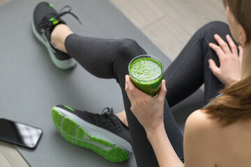 Women's hands tying sport shoes on a gray workout mat. With smoothie for detox in background. Healthy living, dieting lifestyle.