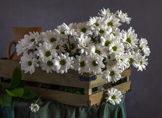 Bouquet of white flowering chrysanthemums in a wooden box and an old ceramic jug
