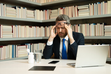 Tired man suffering from headache after computer work, exhausted with closed eyes touching head, relieving pain, migraine. Business problems. Bankruptcy, financial problem and crisis concept.