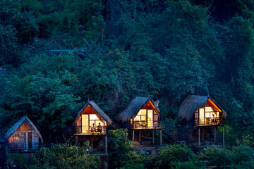 Fototapeta na wymiar Three small wooden houses with lights in the tropical forest