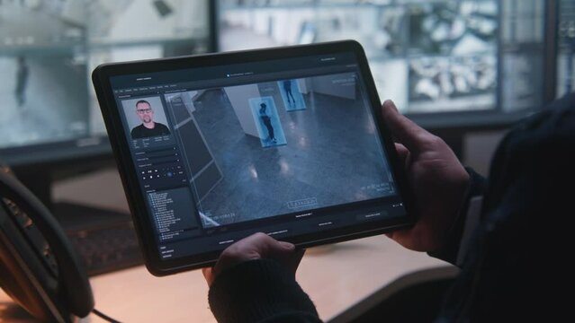 Male security guard controls CCTV cameras in office, uses digital tablet and computers with surveillance camera footage playback on screens. High tech security system. Monitoring and social safety.
