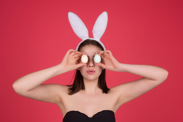 Beautiful young woman with bunny ears and Easter eggs on studio background. Festive bunny and easter eggs season. Stylish woman in Easter bunny ears isolated on studio background.