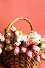 Basket with pastel colored tulips and easter bunnies on pink background. Copy space for text