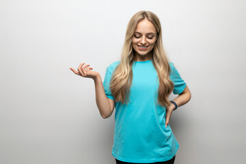 blond young woman in a blue t-shirt points to an empty space on a white background