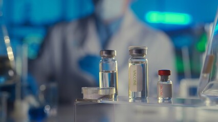 Glass vials with a vaccine on a blurred laboratory background. Bottles with clear liquid and light reflection. Medical background, close up.