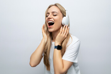 young woman sing along to music from headphones among white background