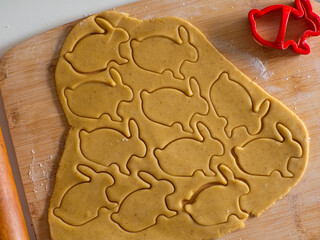 Close-up kneaded ginger dough and carved figurines from it. The shapes of rabbit. Cutting sugar cookie dough with Easter shaped cookie cutters. Preparation for Easter. Holidays baking.